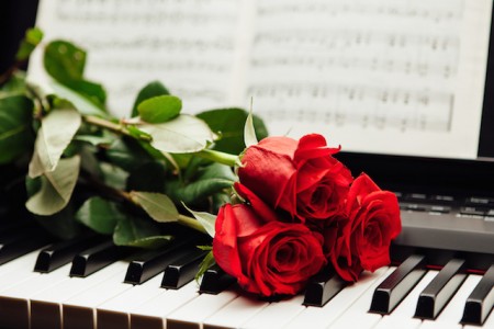 red roses on piano keys and music book